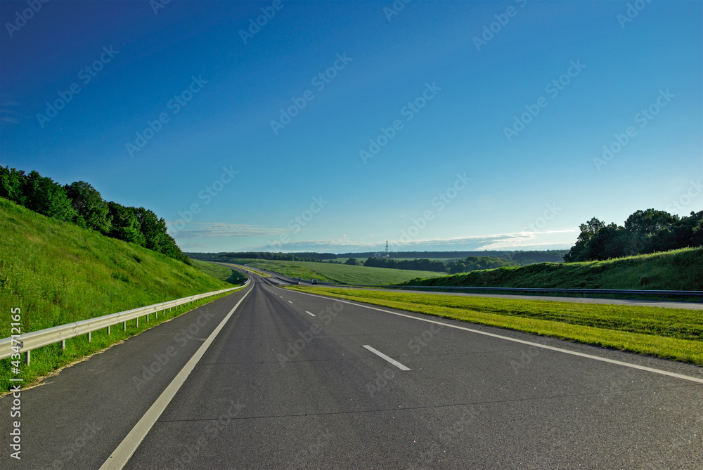 A long highway stretches into the distance under a blue sky and white clouds