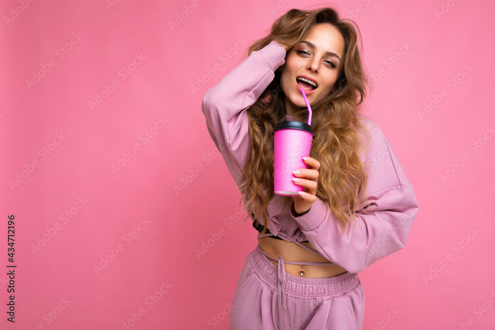 Beautiful sexy young positive brunette woman wearing casual stylish clothes isolated over colorful background wall holding paper cup for mockup drinking coffee looking at camera