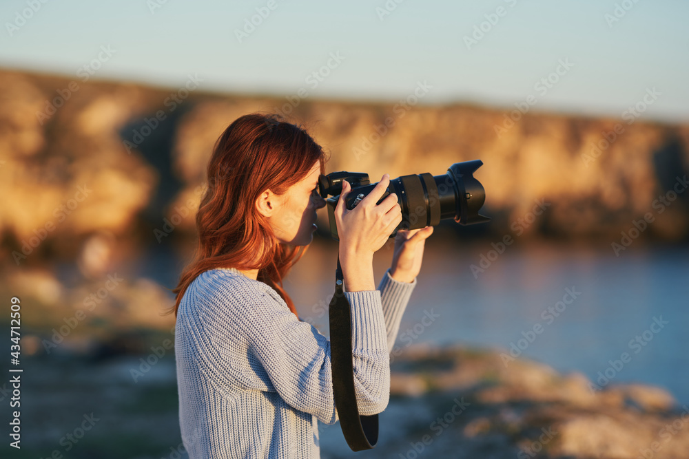 woman with a camera at sunset in the mountains in nature near the sea
