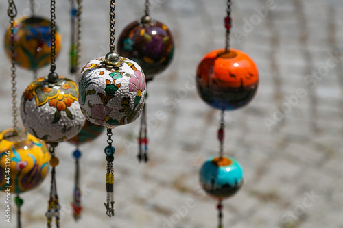 Colorful ceramic pomegranates hanging on long metal chains. Decorative balls with traditional turkish ornaments as souvenirs at street market in Istanbul, close-up, soft focus with copy space area.