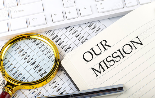 OUR MISSION text on notebook with chart, magnifier,keyboard and pen