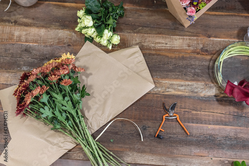 Rear view of a young woman working as florist and creating a beautiful and colourful bouquet with flowers on a wooden table, businesswoman concept.