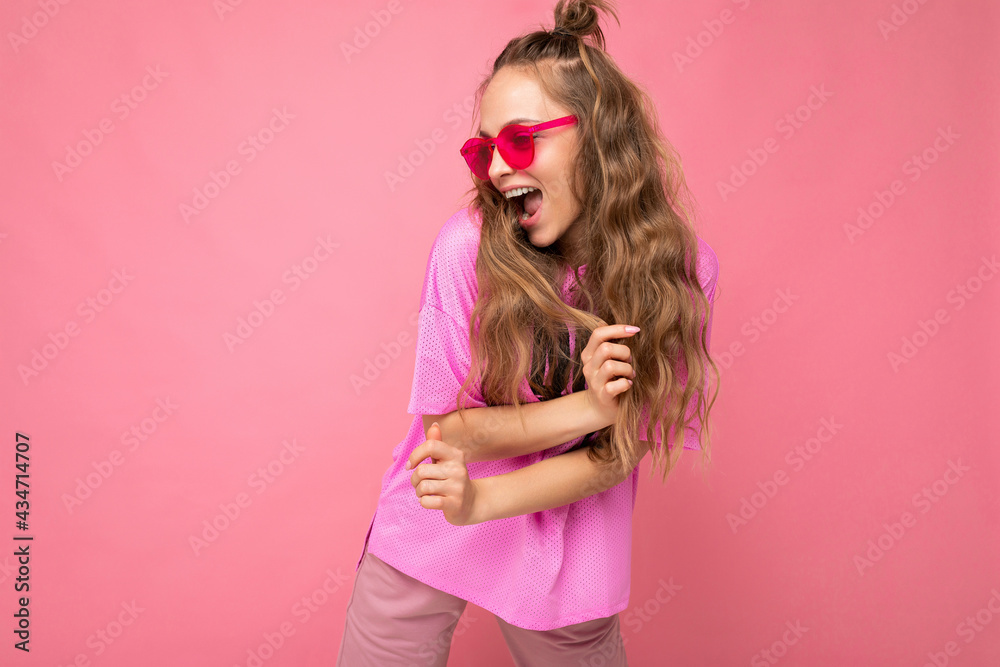 Attractive funny positive joyful young blonde woman wearing everyday stylish clothes and modern sunglasses isolated on colorful background wall looking to the side