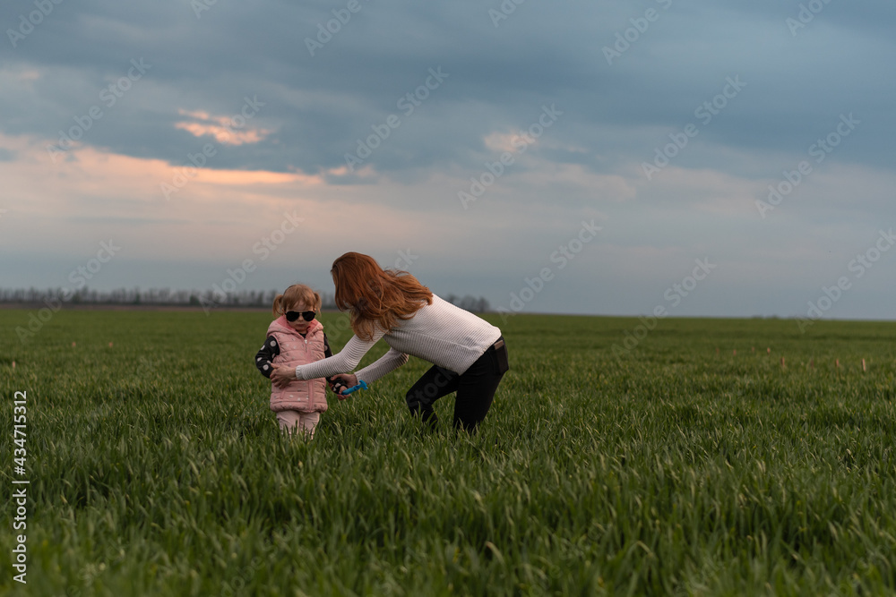 Mom and daughter in green field against evening cloudy sky Mom and daughter in green field against evening cloudy sky