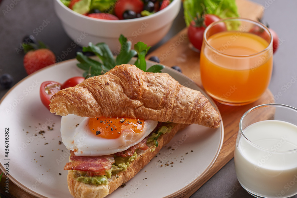 Delicious breakfast with fresh croissants, bacon sandwich with fried egg. milk served, orange juice. strawberry, butterhead, blackberry salad. full american healthy breakfast top view. Delicious breakfast with fresh croissants, bacon sandwich with fried egg. milk served, orange juice. strawberry, butterhead, blackberry salad. full american healthy breakfast top view.