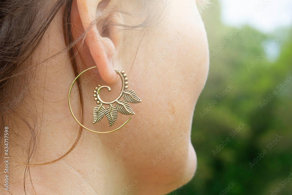 Outdoor detail of female ear wearing metal spiral shape earring