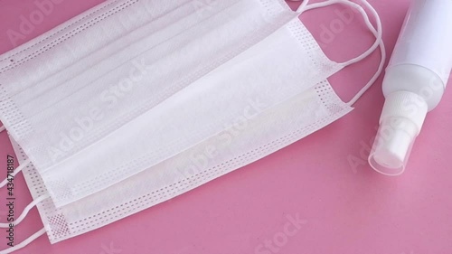 disposable masks, earloop type, with spray alcohol bottle on soft pink surface, slowly movement