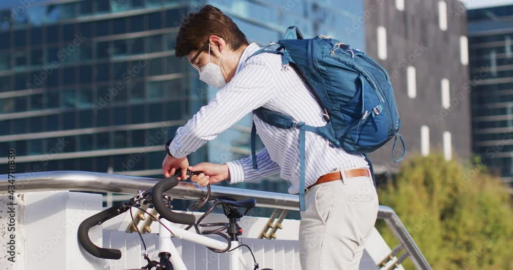 Asian man wearing face mask locking his bicycle at corporate park Asian man wearing face mask locking his bicycle at corporate park