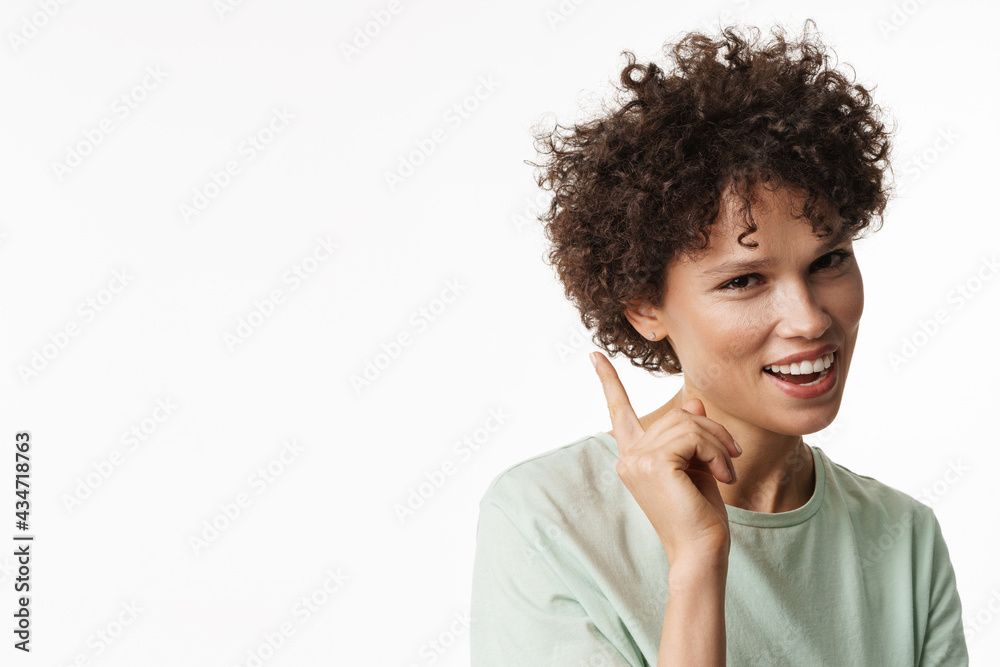 Young curly brunette woman smiling and pointing finger upward Young curly brunette woman smiling and pointing finger upward