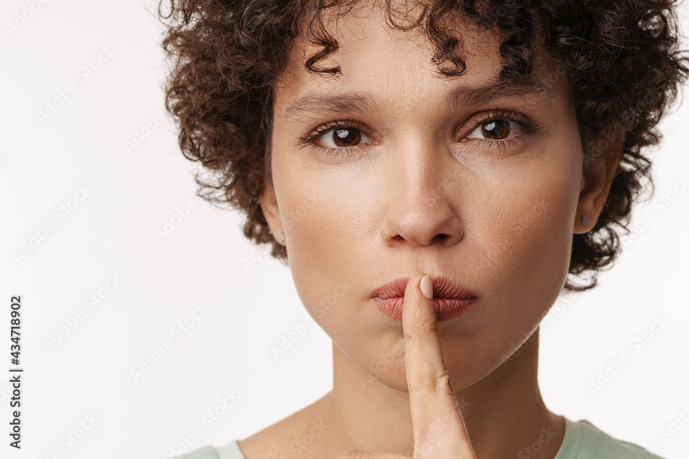Young curly woman looking at camera and showing silence gesture