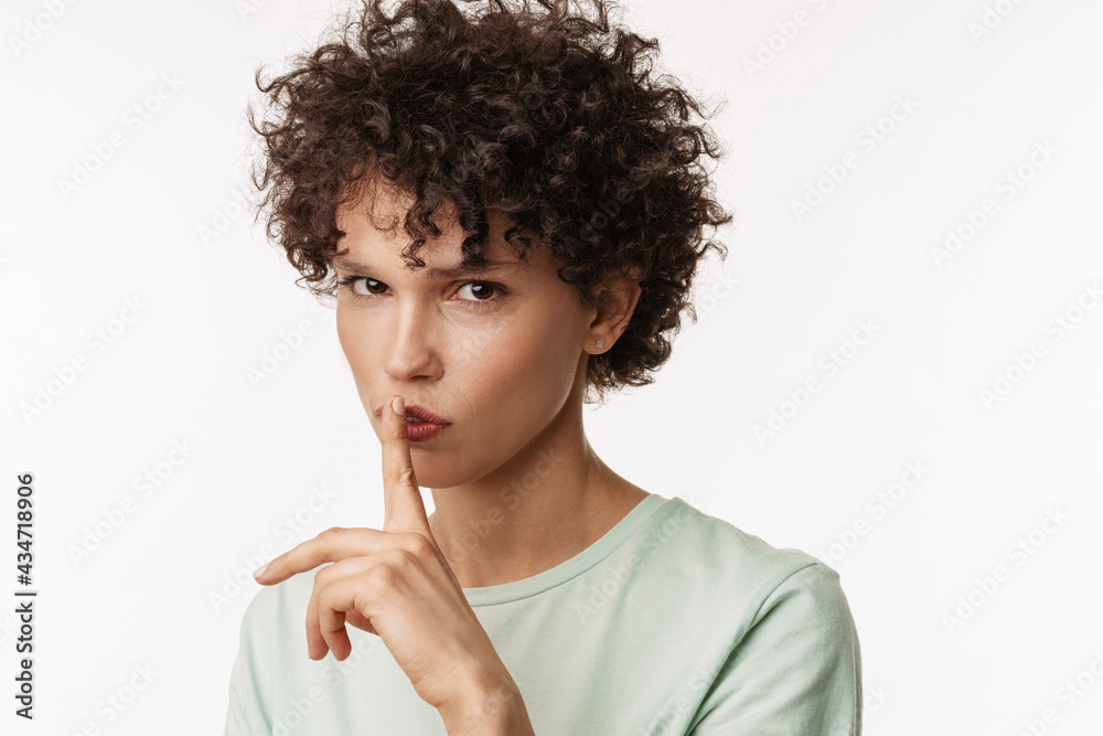Young curly woman looking at camera and showing silence gesture Young curly woman looking at camera and showing silence gesture