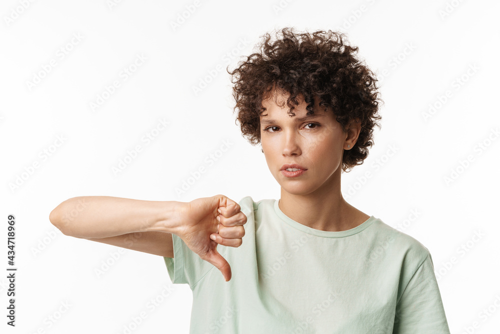 Young curly brunette woman showing thumb down at camera Young curly brunette woman showing thumb down at camera