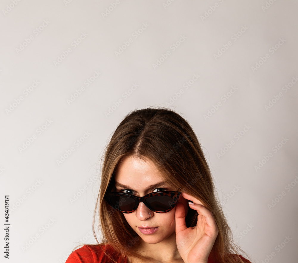 Young attractive woman in red on gray background with copy space. Woman posing with sunglasses. Scar on face. Young attractive woman in red on gray background with copy space. Woman posing with sunglasses. Scar on face.