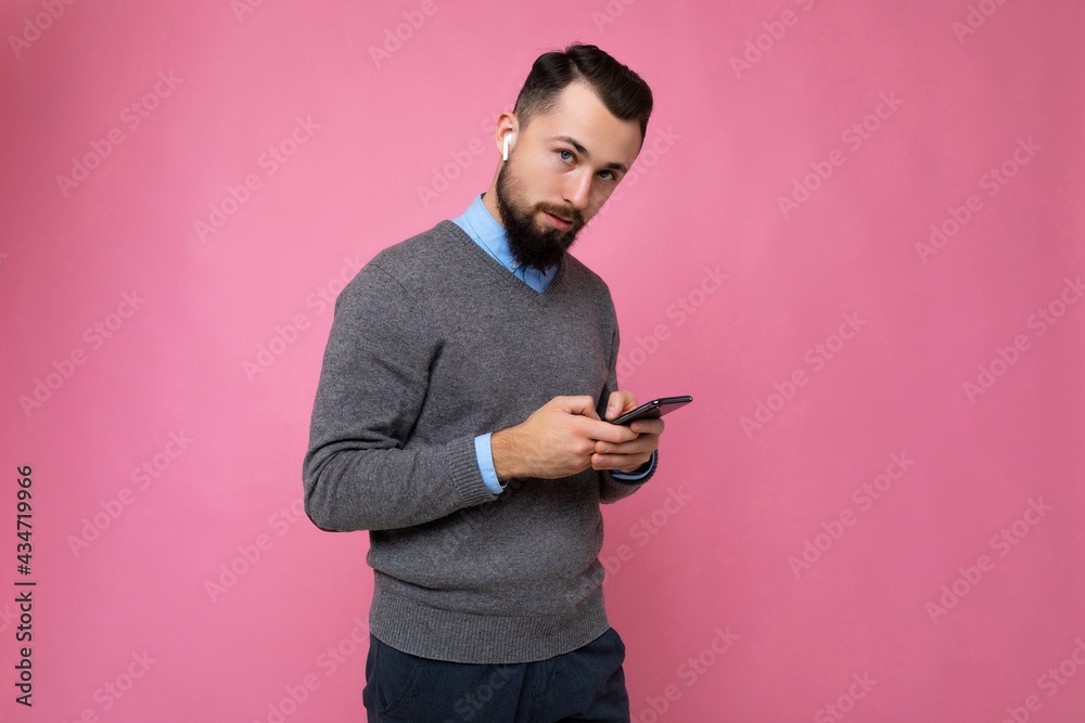 handsome good looking brunet bearded young man wearing grey sweater and blue shirt isolated on pink background with empty space holding in hand and using mobile phone communicating online looking at handsome good looking brunet bearded young man wearing grey sweater and blue shirt isolated on pink background with empty space holding in hand and using mobile phone communicating online looking at