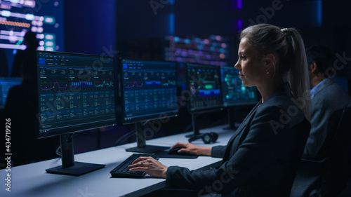 Confident Female Data Scientist Works on Personal Computer in Big Infrastructure Control Room. Team of Stock Market Specialist Use Computers Showing Global Map, Graphs, Charts, Information © Gorodenkoff
