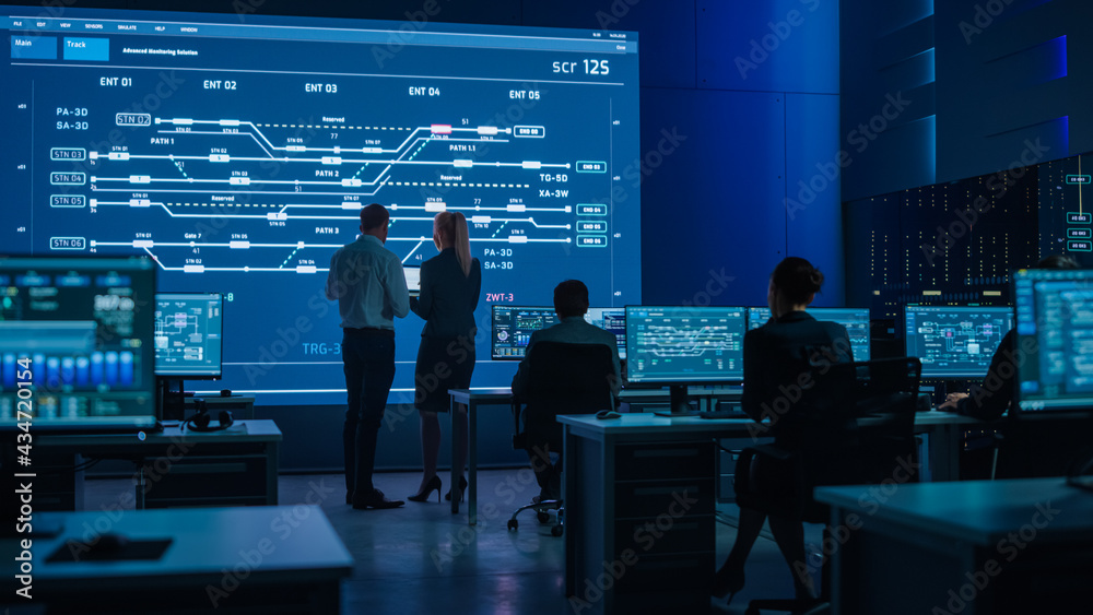 © Gorodenkoff - Telecommunications Company System Control and Monitoring Room with Diverse Multicultural Team of Professionals Working on Computers. Big Screen Display Showing Infrastructure Infographics. Back View
