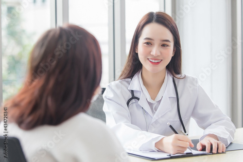 Asian professional doctor female who wears medical coat talks with woman patient to suggest treatment guideline and healthcare concept in office of hospital.