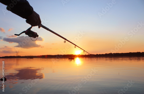 Close-up silhouette of a man's hand holding a fishing rod against the backdrop of a sunset on the river. Evening fishing, ench, crucian carp, rudd