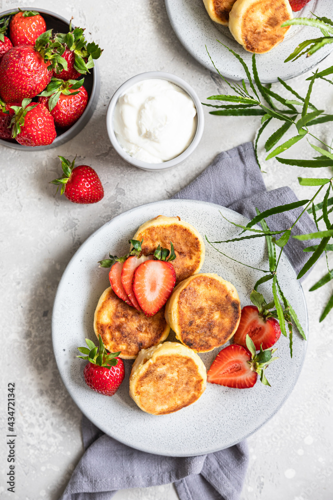 Cottage cheese pancakes or fritters with strawberry and natural yogurt on light grey stone background. Healthy breakfast or lunch. Syrniki. Top view.