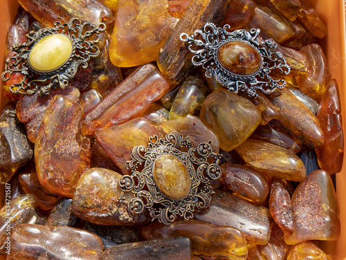Fototapeta Naklejka Na Ścianę i Meble -  Amazing old Baltic amber brooches lie on yellow and orange amber stones. Amber texture, vintage jewelry, energy stone.
