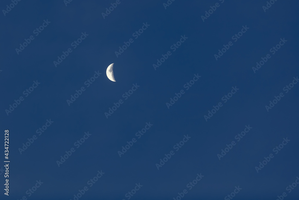 An incomplete disc of the moon in the form of a white crescent against a dark blue cloudless sky An incomplete disc of the moon in the form of a white crescent against a dark blue cloudless sky