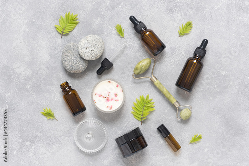 Containers of lotion, essential oils, massage jade roller on a gray concrete background