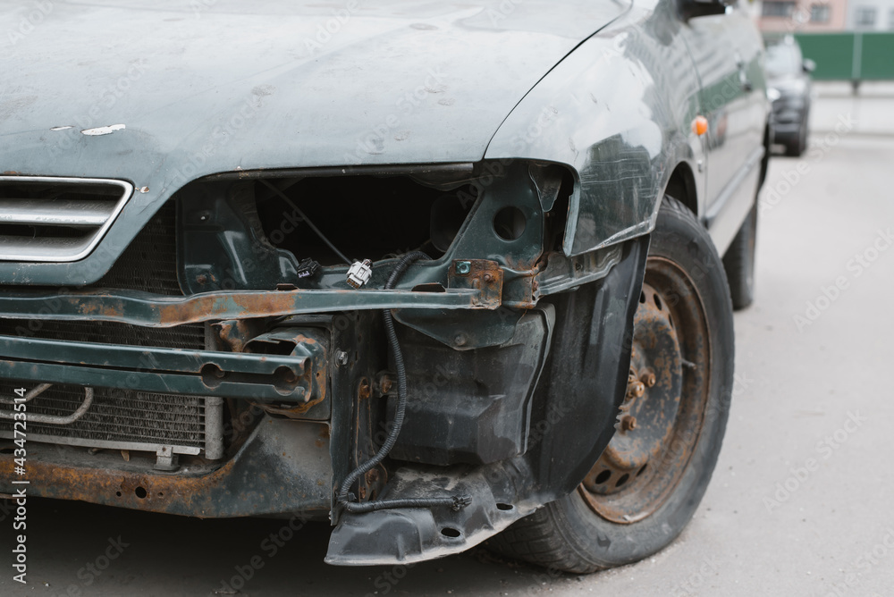 Abandoned, wrecked car. Close-up of destroyed front bumper, headlight and wheel. Broken vehicle after an accident.