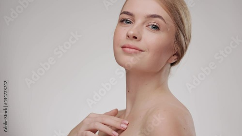 Slow-motion beauty portrait of young woman touching her smooth skin in collarbone area. Skincare concept. Female model with fresh skin smiling at the camera. Close up.