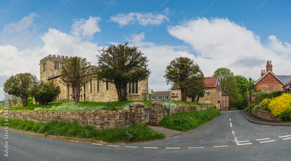 Ancient All Saints Church flanked by dry stone walls under blue sky. Goodmanham, UK.