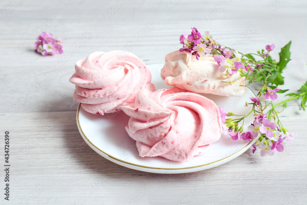 Three marshmallows lie on a plate with delicate pink flowers on a gray background, close-up Three marshmallows lie on a plate with delicate pink flowers on a gray background, close-up