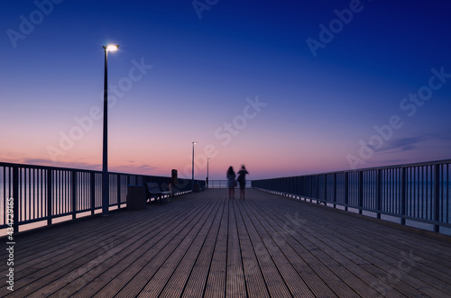 Fototapeta Naklejka Na Ścianę i Meble -  PIER ON THE SEA COAST - Womens walk at a quiet sunset 