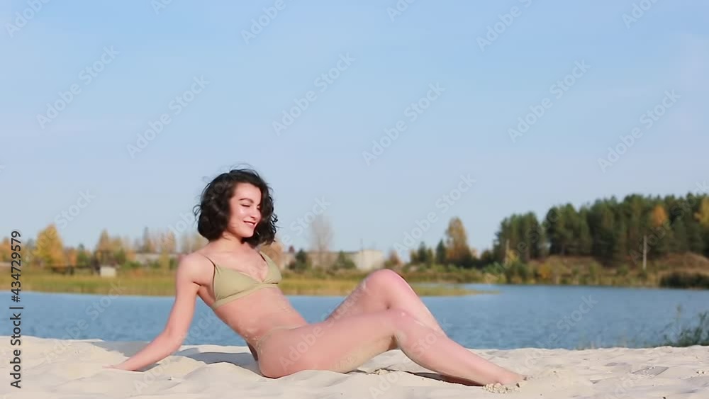 A young beautiful woman in a swimsuit poses for a photographer on the beach near the water A young beautiful woman in a swimsuit poses for a photographer on the beach near the water