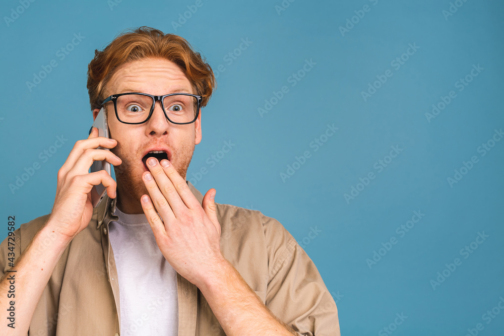 Oh, great news! Smiling shocked amazed young casual man talking on the mobile phone isolated over blue background. Oh, great news! Smiling shocked amazed young casual man talking on the mobile phone isolated over blue background.