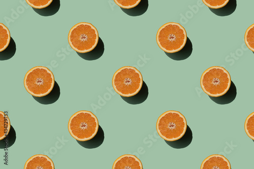 Fruit pattern orange slices on green pastel background. Trendy minimal sunlight summer cocept.