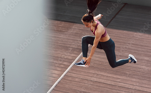 View from above full-length shot of an athlete woman sprinting in the city on a sunny day. Fitness girl in sportswear duing training exercises for running outdoors.