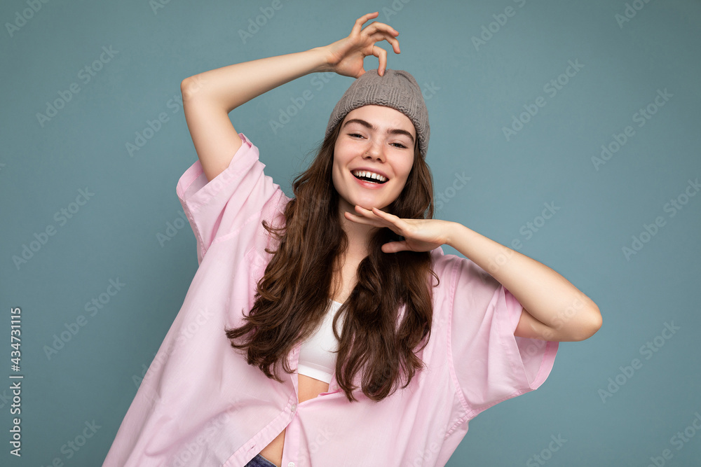 Attractive smiling happy young brunette woman standing isolated over colorful background wall wearing everyday stylish outfit showing facial emotions looking at camera