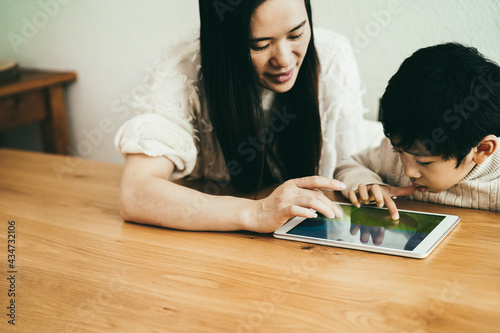 Asian mother and little son playing video games with tablet at indoors at home - Focus on boy face photo