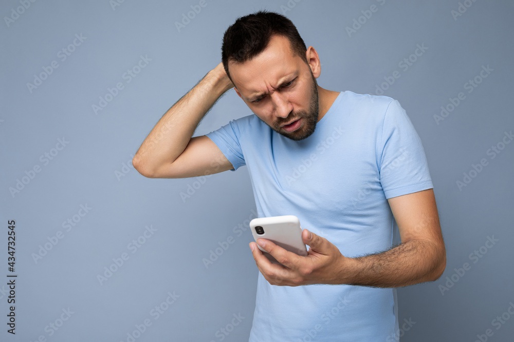 Photo shot of handsome don't understanding asking good looking young man wearing casual stylish outfit poising isolated on background with empty space holding in hand and using mobile phone messaging Photo shot of handsome don't understanding asking good looking young man wearing casual stylish outfit poising isolated on background with empty space holding in hand and using mobile phone messaging