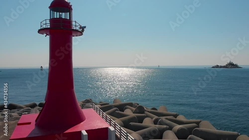 Sea surface is glittering reflects sun lights. Red lighthouse is on wave breakers. Beautiful nature aerial drone footage took with 4K 30fps.