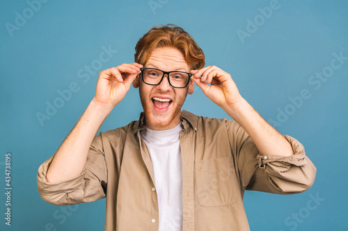 Headshot of attractive red-haired caucasian young business man wearing casual and glasses, isolated on blue background.