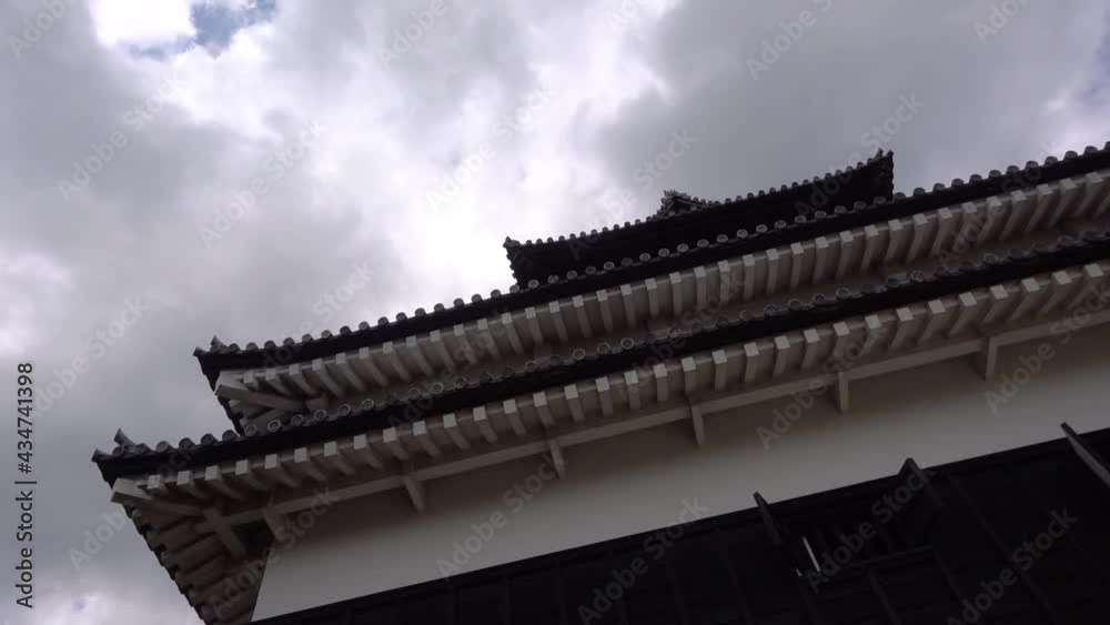Slow motion rotating shot looking up at Japanese Castle against cloudy sky Slow motion rotating shot looking up at Japanese Castle against cloudy sky