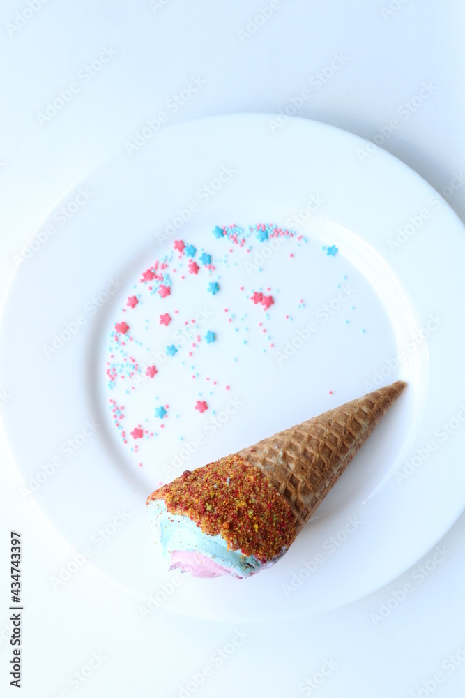 Obraz premium Ice cream cone with pink and blue sugar sprinkles on a white plate