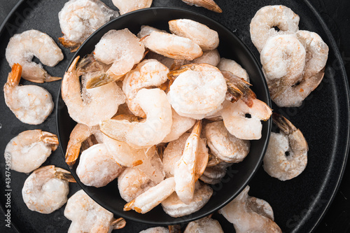 Frozen peeled boiled prawns, in bowl, on black stone background, top view flat lay