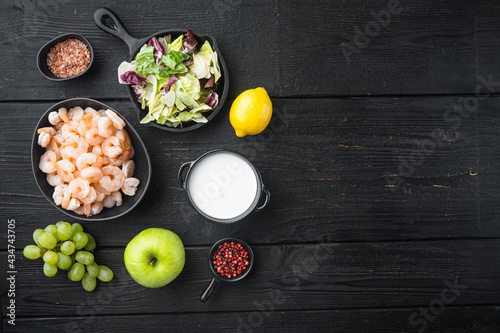 Fresh summer vitamin appetizer of green salad, shrimps, olive ingredients, with sauce apple and grape, on black wooden table , top view flat lay, with copy space for text