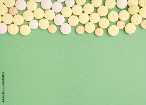 Pile of tablets medicine for people's health to heal diseases isolated on a green background. Space for text. Top view. Healthcare and medical concept