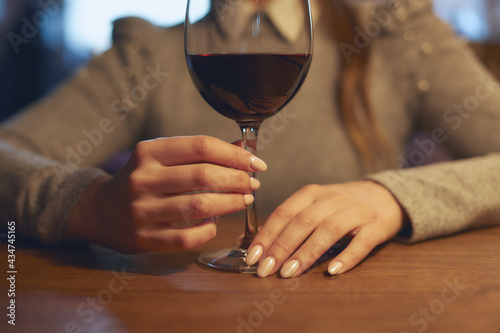 Hand of a young beautiful woman holding a glass of wine indoors of a stylish wine restaurant