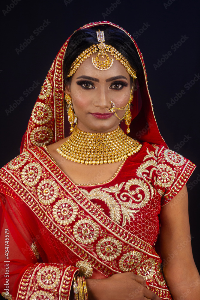 Young attractive Indian female model dressed in traditional Indian lehenga choli costume with Kundan style jewelry. Looking down. Black background