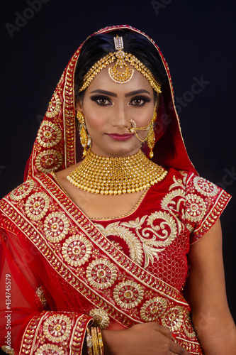 Young attractive Indian female model dressed in traditional Indian lehenga choli costume with Kundan style jewelry. Looking down. Black background