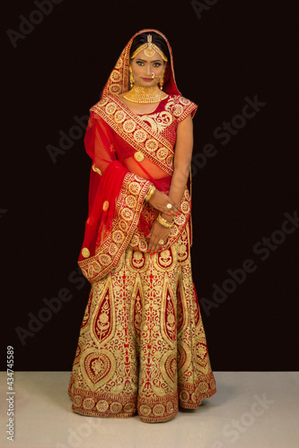 Young attractive Indian female model dressed in traditional Indian lehenga choli costume with Kundan style jewelry. Looking down. Black background photo