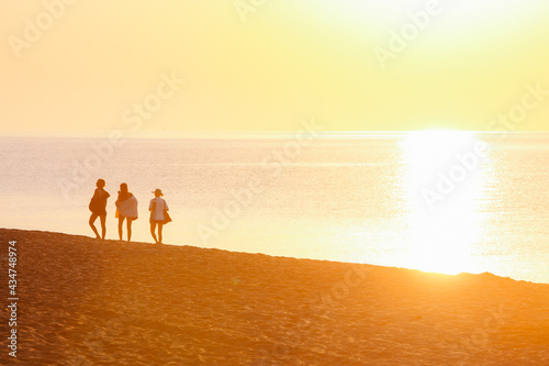 group of friends walking by sandy beach on sunset